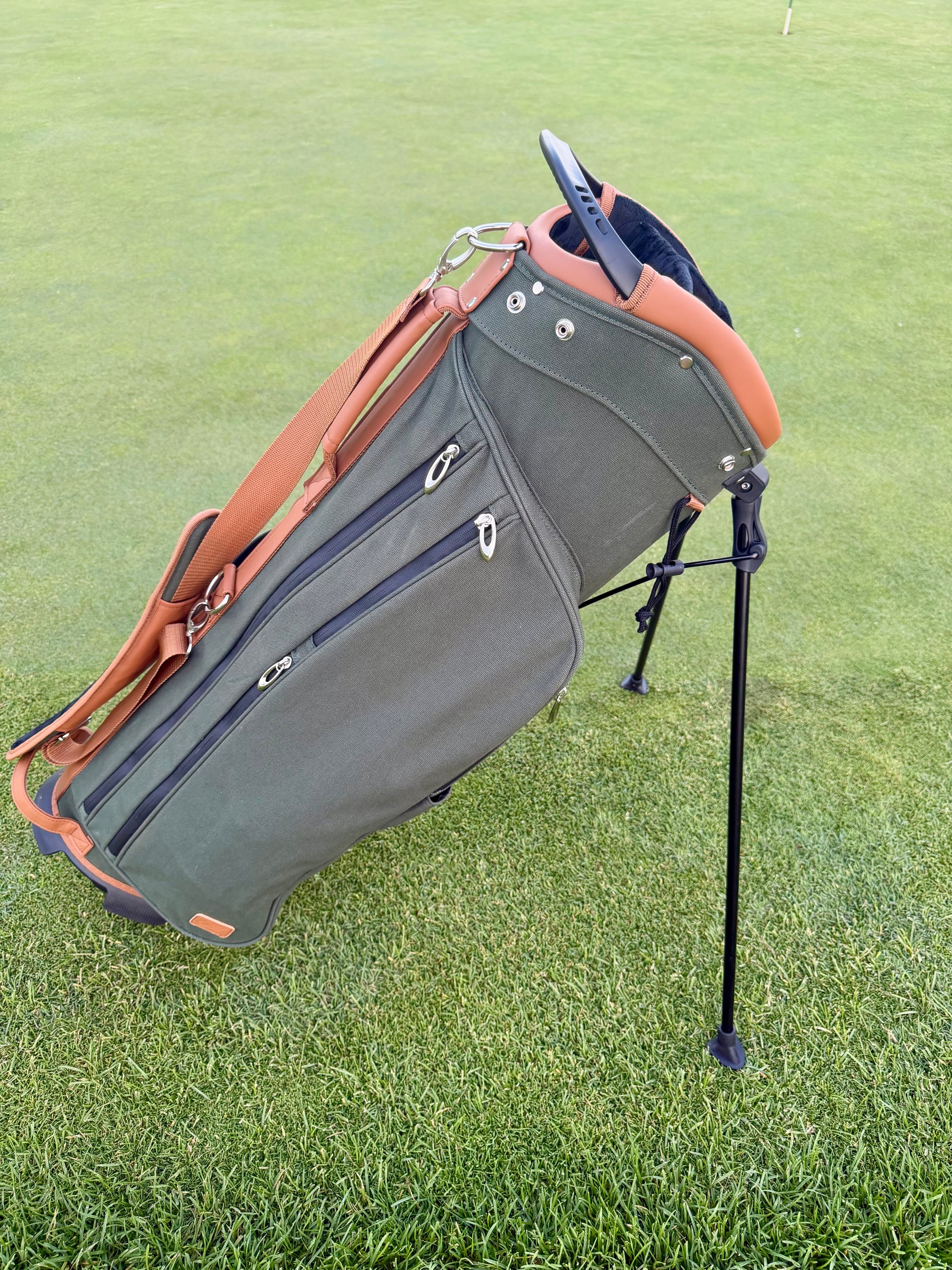 Green golf bag with brown accents on a grassy background