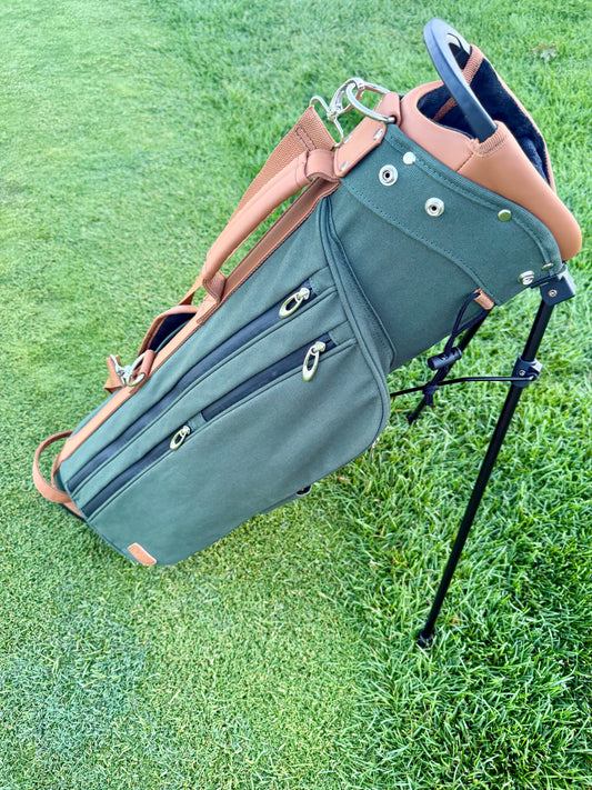 Green golf bag with brown leather straps on a grassy background